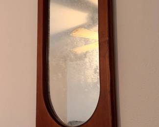 Wood-framed wall mirror with an elongated oval mirror, scalloped top, and small curved display shelf. Warm brown finish with dark trim around the glass.