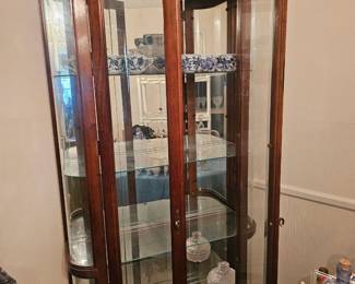 A tall wooden illuminated curio cabinet with curved glass sides.