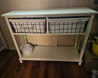 A white wooden entryway console table with two wire storage baskets.