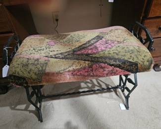 An antique cast iron vanity bench with tapestry upholstery.