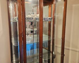 A tall wooden illuminated curio cabinet with curved glass sides.