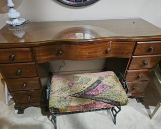 A mid-20th-century wooden serpentine-front vanity desk with glass top.