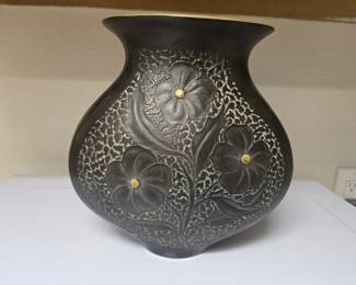 Elevate your mid-century or brutalist decor with this striking, collectible Freeman & McFarlin California art pottery vase. Molded in a highly desirable, bulbous squat silhouette, this piece is cataloged as model #318. Moving away from their typical high-shine gold finishes, this rare variation features a velvety matte charcoal/black body accented by exquisite brushed-bronze and gold floral carvings. The central dogwood-style blossoms are deeply embossed against a heavily textured, chiseled background. The bottom is fully marked with the impressed mold number, the official foil manufacture stamp, and the iconic cursive incised signature of the designer, Anthony