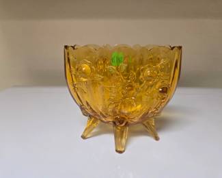 Add a touch of warm, mid-century elegance to your home with this striking vintage Fenton art glass bowl. Rendered in a glowing amber-gold colorway, it features the highly collectible "Cabbage Rose" embossed floral design, a gently scalloped rim, and three classic structural peg feet. The glass boasts incredible color depth that beautifully catches and filters natural light. A wonderful standalone accent piece, candy dish, or thoughtful gift for a vintage glass enthusiast. Excellent vintage condition with no visible damage.