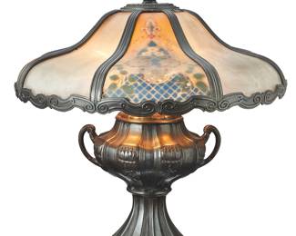 3203 An American reverse painted lamp Early/mid-20th century The patinated metal urn-formed base issuing three lights with updated fixtures, surmounted by a glass and metal shade painted with floral motifs, electrified Unmarked Height of lamp 23 in., width 11 3/4 in., depth 9 in.; height of shade 7 1/2 in., diameter 21 1/2 in. Estimate: $300 - $500