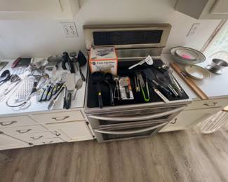 kitchen utensils: boxed Norpro pasta machine, Farberware pizza cutter, ladles, spatulas, tongs, whisks, graters, knives, scoops, and serving spoons, plus pasta bowls