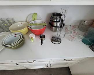 yellow and green nesting mixing bowls, set of 4 plastic mixing bowls with lids, stainless steel mixing bowls, measuring cups, Pyrex measuring cups, and paper towel holder