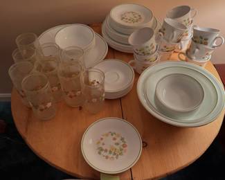 Corelle Strawberry Sundae vitrified glass dinnerware collection displayed on a round wooden table alongside matching glass tumblers and coffee mugs