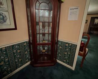 lighted Queen Anne style corner curio cabinet with glass-mullioned doors, filled with Fostoria clear pressed glassware.