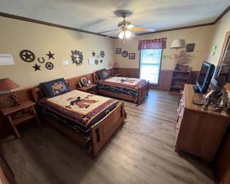 A. Brandt Ranch Oak Western-themed bedroom: pair of wood twin beds with cowboy bedspreads and shams, matching nightstands and dresser, bookcase, lamps, and Western wall décor (metal stars, horseshoes, and horses)