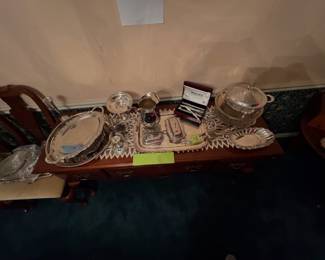 Queen Anne five-foot sideboard displaying an assortment of silverplate serving trays, hollowware, a silver pitcher, and a boxed flatware set