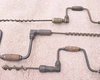 three antique hand drills bit braces (hand-cranked woodworking tools used to borep holes) paired with spiral augerdripll bits 