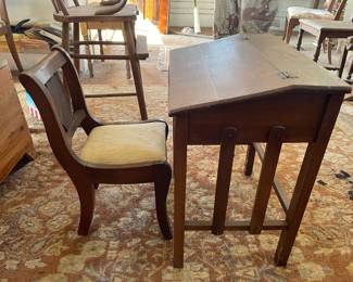 1910-1930 This is a vintage wooden school desk featuring a hinged slanting top and an attached chair with an upholstered seat. The piece displays a warm medium-brown wood finish with visible grain and simple square legs.
