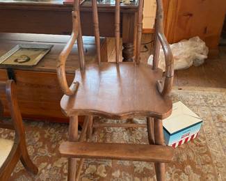 Antique Windsor High Chair 1880-1920 A wooden high chair featuring a Windsor-style spindle back, bentwood arms, a shaped seat, and an integrated footrest supported by four splayed legs. The piece displays a medium brown finish with visible wood grain and construction screws on the arm joints.