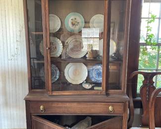 This is a vintage mahogany china cabinet featuring a glazed upper display section with glass doors and side panels enclosing wooden shelves currently holding decorative plates. The lower section consists of a long drawer over a double-door cabinet base, accented with brass ring pull hardware.