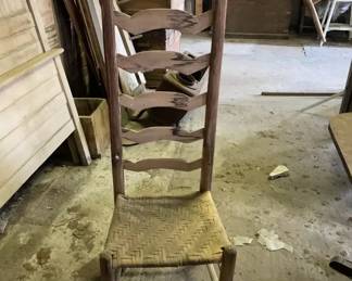 1780-1820 Ladder back chair This antique ladderback chair features a tall backrest with five arched horizontal slats and acorn-finial rear posts. The seat is woven from rush material in a herringbone pattern, supported by plain cylindrical legs connected by simple stretchers.