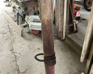 1880-1920 Antique Hand Corn Planter This is a vintage wooden hand corn planter featuring a cylindrical wooden body with aged red paint remnants, a metal plunger mechanism, and rusted iron fittings and rings attached at the top and bottom.