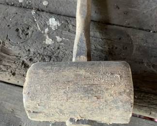 1880-1920 Antique Wooden Mallet A heavy vintage wooden carpenter's mallet featuring a thick cylindrical head and a shaped handle secured through the head with a wedged tenon. The tool displays a raw, unfinished surface texture with visible grain and minor surface debris.