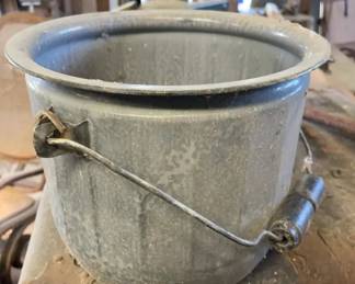 Graniteware Berry Bucket 1880-1920 A cylindrical metal bucket coated in gray mottled enamelware featuring a wire bail handle with a wooden grip and a rolled rim. The surface shows visible dust and minor wear typical of age and use.