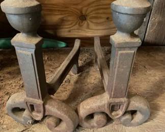 Andirons 1900-1920 A pair of heavy cast iron fireplace andirons featuring scrolled feet, rectangular columnar shafts, and acorn finial tops. They display a dark oxidized metal finish with traces of surface rust.