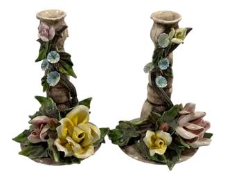 2025 - Pair Capodimonte Candleholders 8" (Description): A set of two ceramic candleholders featuring  applied floral decorations. Each candleholder  stands 8 inches tall and is adorned with  hand-formed roses and morning glories in  pastel hues of pink, yellow, and blue, accented with green leaves climbing up the  stem.