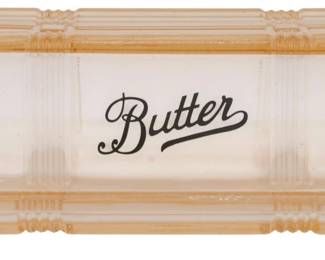 144 - Pink Glass Butter Dish 2.5"x6.5"x3" (Description): Pink depression-style glass butter dish with  cover. The lid features the word "Butter" in  elegant black script lettering on a frosted  white panel. The dish has a ribbed Art Deco  design with scalloped edges on the base tray. Measures 2 1/2" x 6 1/2x 3".