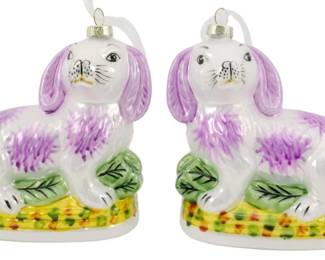 244 - Pr Blown Glass Staffordshire Rabbit Ornaments (Description): A charming pair of Danny's Fine Porcelain  Staffordshire dog ornaments. These decorative  glass ornaments depict recumbent spaniels in  the classic Staffordshire style, featuring  white bodies with purple accents on the ears and fur, resting on colorful yellow and green  bases with foliate details. Each ornament is  fitted with a silver cap and hanging loop  for display. Measures 5 inches.