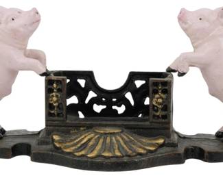 85 - Cast Iron Pig Business Card Holder 5"x11"x3" (Description): Cast iron business card holder featuring two  charming pink painted pigs standing upright  on their hind legs, flanking a decorative  pierced center compartment. The piece rests  on an ornate black and gold painted base with a scallop shell motif. The open work  fence-style center section features floral  accents with gold highlighting. Measures 5  inches high by 11 inches wide by 3 inches  deep.