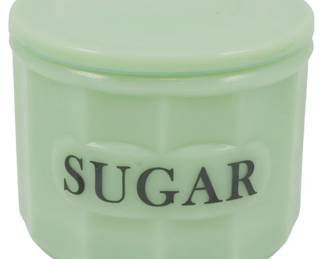 156 - Jadeite Sugar Container w/ Lid 4.5"x4.5" (Description): Jadeite sugar container with lid, featuring  the classic pale green opaque glass  characteristic of jadeite kitchenware. The  container displays the word "SUGAR" in black  lettering on a raised panel design. Includes matching jadeite lid. Measures 4 1/" x 4.5".