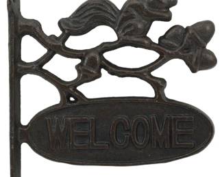120 - Cast Iron Squirrel Welcome Wall Sign 8"x7.5" (Description): Cast iron wall sign featuring a squirrel  perched on an oak branch with acorns, above  an oval plaque reading "WELCOME." The sign  has a dark brown finish with a vertical  mounting bracket with two screw holes. Measures 8 inches by 7.5 inches.
