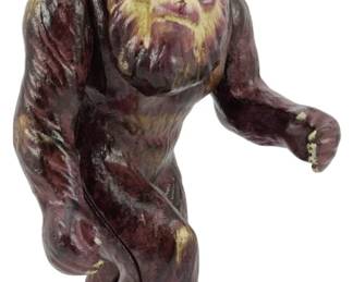 128 - Cast Iron Bigfoot Bank 7.5" (Description): Cast Iron Bigfoot Bank measuring 7.5 inches  tall. This charming coin bank depicts the  legendary Sasquatch in a striding pose, cast  in solid iron with details in brown and tan  tones highlighting the creature's fur and facial features.