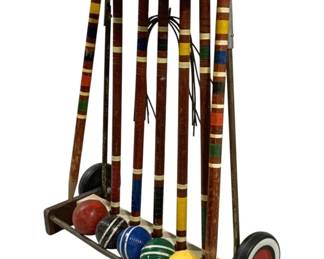 2123 - Vintage Croquet Set 22"x29"x10" (Description): Vintage croquet set complete with rolling  cart stand. The set includes six wooden  mallets with colorful striped handles, five  croquet balls, and wickets. Measures 22" x  29" x 10".