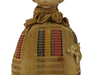 256 - Vintage Bisque Head Pin Cushion Doll 8" (Description): Vintage bisque head pin cushion doll  featuring a molded blonde-haired girl with a  pink ribbon bow in her hair. The doll has  painted facial features with blue eyes and  rosy cheeks. The fabric body forms a functional pin cushion dressed in tan woven  fabric with colorful striped panels in red,  gold, and dark green. The cushion is trimmed  with delicate lace at the collar and hem.  Measures 8 inches tall.