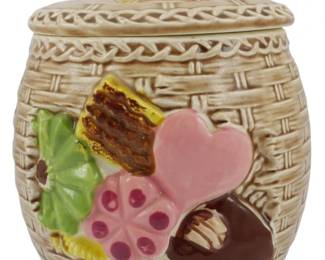 254 - Vintage Napco Basketware Cookie Jar 8"x10" (Description): Vintage Napco Basketware cookie jar featuring  a charming basketweave design in a tan  finish. The jar is decorated with colorful  molded cookies including a pink heart-shaped  cookie, a pink flower cookie with polka dots, a green pinwheel cookie, a brown  honeycomb-textured cookie, and chocolate  candies. The lid is topped with a decorative  finial of miniature cookies including a pink  frosted cookie and a yellow treat. Measures 8