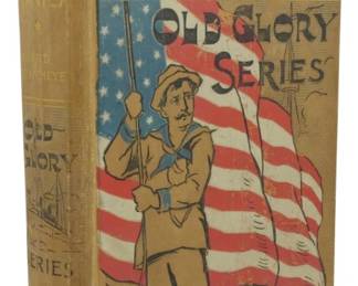 25 - 1898 1st Ed. Under Dewey at Manila (Description): First edition of Under Dewey at Manila by  Edward Stratemeyer, published in 1898. This  volume is part of the Old Glory Series. The  decorative cloth binding features a patriotic  design with a sailor holding the American flag, rendered in olive, red, white, and  blue. The front cover displays a gilt  portrait medallion of Admiral Dewey at the  top. The spine is similarly decorated with  the title and series name.