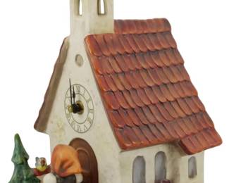170 - Hummel Chapel Time Clock #442 Figure 12" (Description): Depicting a charming Bavarian-style church  with an onion dome bell tower, terra cotta  colored tile roof, and working clock face. A  Hummel girl figure stands at the arched  doorway, with a small evergreen tree and colorful flowers adorning the base. Measures  12 inches tall.