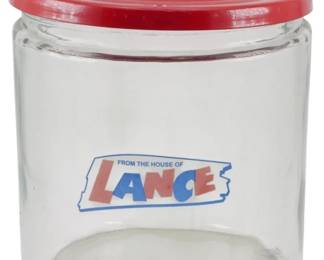 109 - Lance Glass Store Jar w/ Red Metal Lid (Description): Lance glass store jar featuring the classic  "From the House of Lance" logo in red and  blue on the front. The cylindrical jar comes  with a red metal lid with a knob finial.  These counter display jars were commonly used in general stores and service stations to  display Lance snack products. Measures 10" x  8".