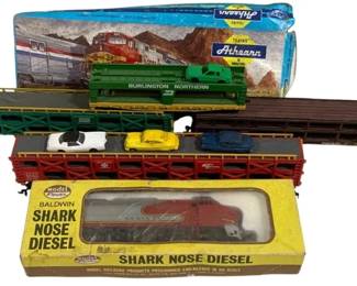 1665 - Assorted HO Scale Train Cars (Description): A collection of six HO scale train cars  including a Model Power Baldwin Shark Nose  Diesel locomotive in original box, an Athearn  Burlington Northern boxcar in original  packaging, a green Burlington Northern gondola car, a brown flatbed car, and an auto  transport car carrying miniature vehicles. A  varied assortment suitable for model  railroad enthusiasts.