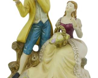 1084 - Porcelain Courting Couple Figurine 8" (Description): Porcelain figurine depicting a romantic  courting couple in 18th century attire. The  gentleman stands playing a flute, dressed in  a yellow coat with blue breeches, while the  lady sits beside him in a burgundy bodice and flowing yellow skirt, holdinga basket of  flowers. The pair is positioned on a  naturalistic base with tree stump details and  subtle yellow accents. The piece has a soft  matte bisque finish with delicate