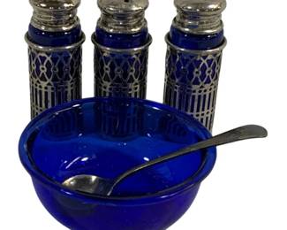 2321 - 4 Cobalt Blue Glass Silverplated Items (Description): A four-piece set of blue glass items with  silverplated accents. The collection includes  shakers with pierced silverplated sleeves  and tops, along with a blue glass bowl  accompanied by a silverplated spoon.