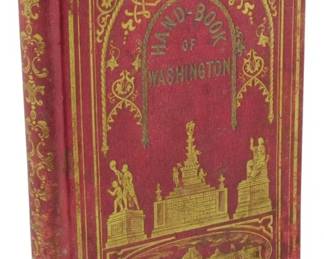 6 - 1854 Ed. Bohn's Hand-Book of Washington (Description): 1854 edition of Bohn's Hand-Book of  Washington. The book features a decorative  red cloth binding with elaborate gilt  embossing on the front cover, depicting  Washington monuments and the Capitol building. The spine and cover show gilt  ornamental borders and scrollwork typical of  mid-19th century American publishing. The  binding exhibits age-appropriate wear with  rubbing to the edges and corners.