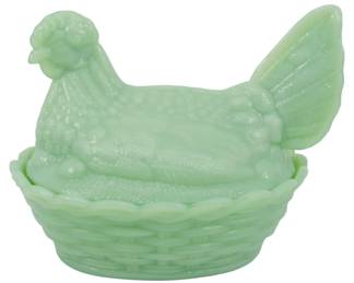 149 - Jadeite Hen on Nest 5"x7"x5" (Description): Jadeite glass hen on nest covered dish  featuring a detailed rooster lid seated atop  a woven basket-style base. The translucent  green milk glass displays the characteristic  soft jade coloring popular in vintage American glassware. The hen figure shows  finely molded feather details, while the base  mimics a traditional woven basket pattern.  Measures 5 inches tall by 7 inches long by 5  inches wide.