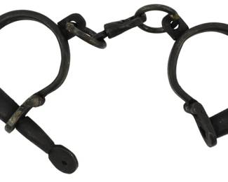 188 - Antique Style Cast Iron Handcuffs w/ Chain (Description): Cast iron handcuffs featuring a traditional  D-shackle design connected by a chain link.  The handcuffs display a dark patinated finish  and operate with pin-style locking  mechanisms. The heavy construction and aged appearance suggest period or reproduction  restraints in the style of 19th century law  enforcement equipment.