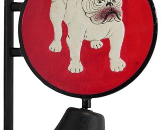 162 - Cast Iron Bulldog Bell 13"x10" (Description): Cast iron bulldog bell featuring a  wall-mounted design with a circular medallion  displaying a white bulldog against a vibrant  red background. The black iron frame  includes a mounting bracket on the left side and a bell suspended below the medallion.  Measures 13 inches by 10 inches.