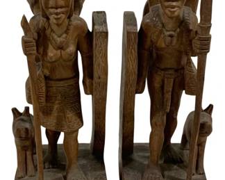 2020 - Pair Carved Wood Figural Bookends 12" (Description): A pair of carved wood bookends featuring  figural designs. Each bookend depicts a  standing figure holding a spear, accompanied  by a small animal at the base. The pieces  showcase detailed carving work including traditional dress and geometric patterns on  the bases. Measures 12 inches in height.