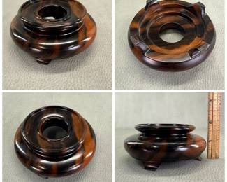 A circular, turned wood display base of polished hardwood with pronounced grain patterns, supported by four small feet on the bottom; approximately 2 inches tall.