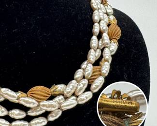 Closeup of the vintage Miriam Haskell three-strand faux pearl necklace featuring rice or baroque-shaped glass pearls accented by ribbed, melon-shaped gold-tone beads and decorative petal caps. 14” length; Miriam Haskell stamp on the clasp.