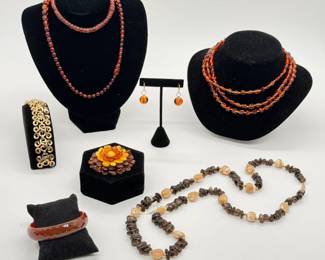 A natural Baltic Amber floral brooch featuring stacked petals in yellow, cognac, and dark brown or cherry tones; a Crown Trifari gold-tone swirl link bracelet; real amber beaded necklaces, amber bead drop earrings; and a vintage root-beer-colored faceted Bakelite bangle bracelet