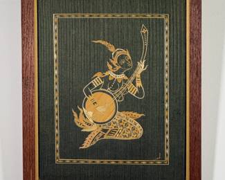 A vintage straw or corn husk marquetry wall art depicting a traditional Thai or Asian celestial musician or dancer playing a stringed instrument against a textured dark background. Framed size 14"W x 17"H.