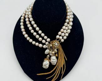 A vintage unsigned Miriam Haskell statement necklace –  three-strand high-luster, ivory-toned faux baroque pearls with ornate focal clasp medallion heavily detailed with an intricate gold-tone filigree backing, clear rhinestones, and delicate hand-wired accents. Two large dangling baroque pearl pendants suspended beneath the rhinestone centerpiece.